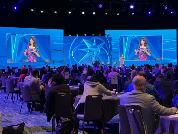 Antoinette Griffin speaking in front of two large TVs